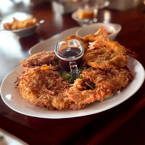 Golden fried potato pancakes arranged on a white plate with a small bowl of dark sauce in the center, garnished with fresh herbs