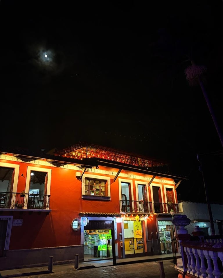 Night view of a bright orange building with illuminated storefront and shops on the ground level beneath a dark sky with moon visible